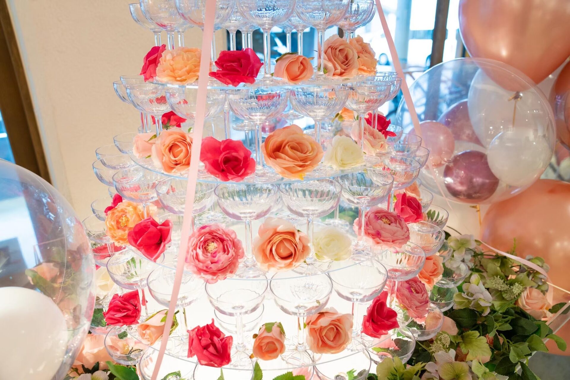 Round champagne tower with flowers laid out on each tier along with a glass.