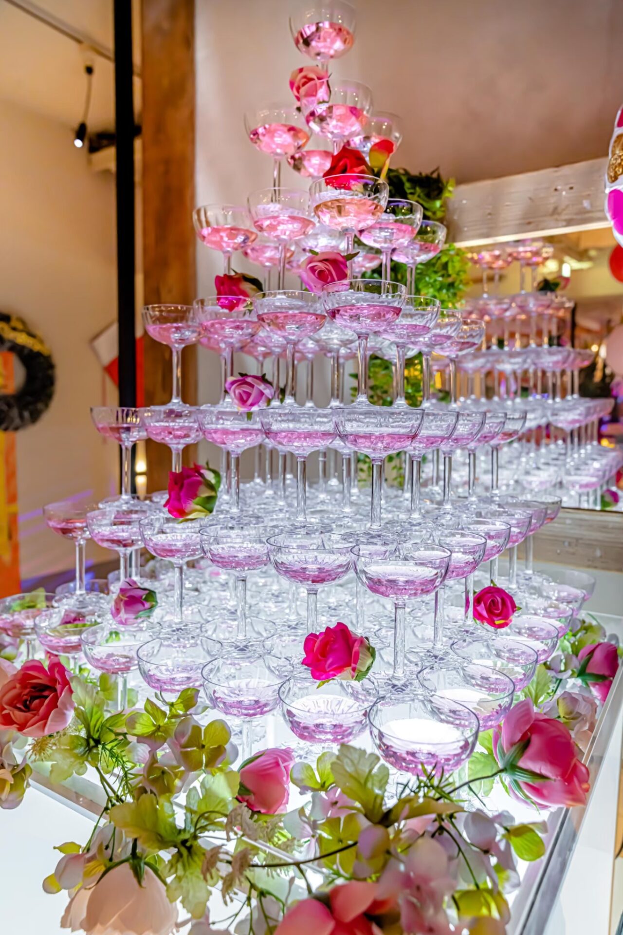 Champagne tower with pretty pink flowers and glasses inside.
